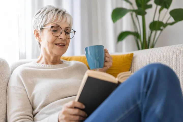 Ältere Frau liest entspannt mit einer Tasse Tee auf dem Sofa