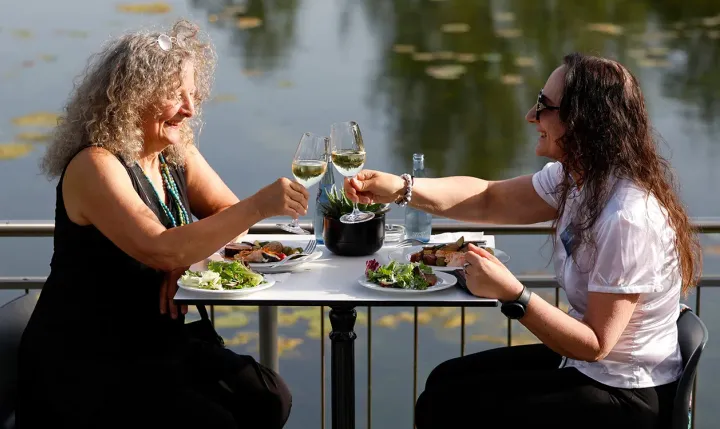 Zwei Frauen genießen entspannt ihr Essen am Wasser und stoßen an
