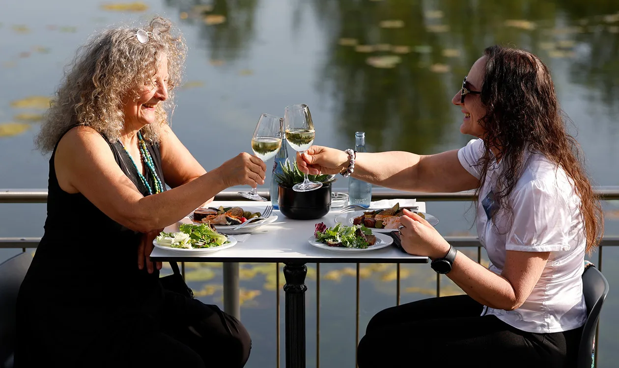 Zwei Frauen genießen entspannt ihr Essen am Wasser und stoßen an